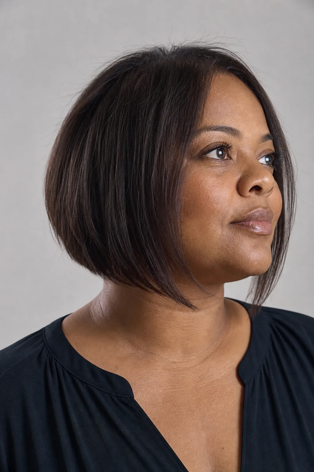 Angled A-line bob longer at the front framing the jaw on fine dark-brown hair, woman with a fuller round face
