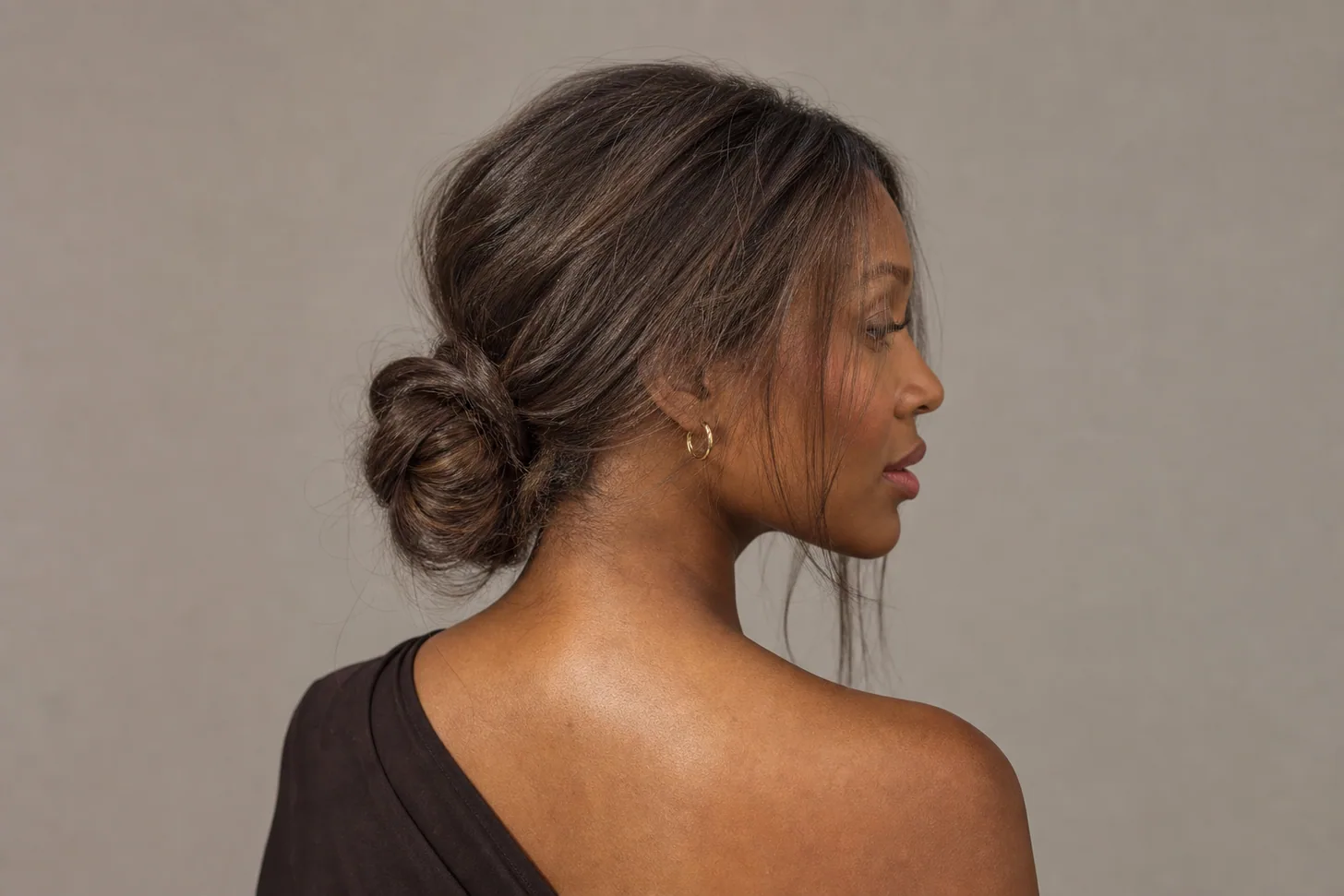 Mid-height looped bun spread wide and soft with crown height on fine mid-brown hair