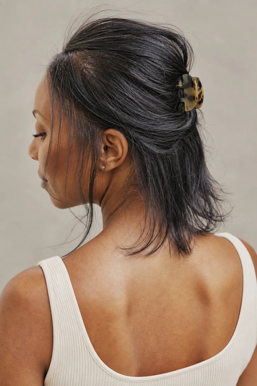 Fine collarbone-length hair in a small half-up twist secured with a claw clip, soft pieces left at the front, rear three-quarter view