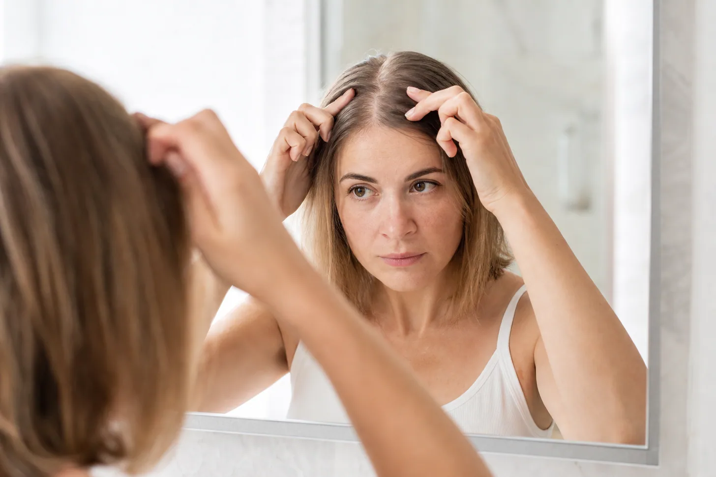 Woman parting her fine hair in a mirror to look at the width of her part