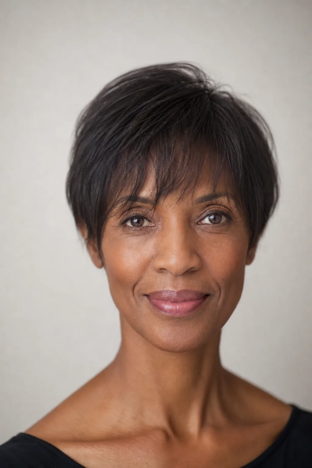 Fine hair in a pixie with the weight kept low and soft width over the ears, plus a forehead fringe, long face, front view