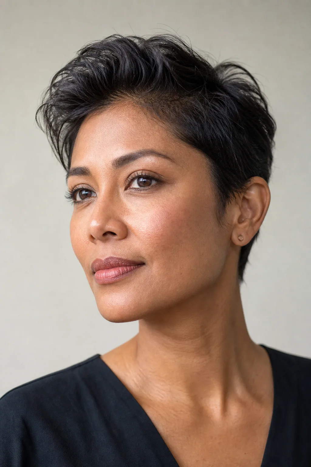 Classic pixie with a soft lifted quiff at the front and tapered sides on fine dark hair, woman with an oval face